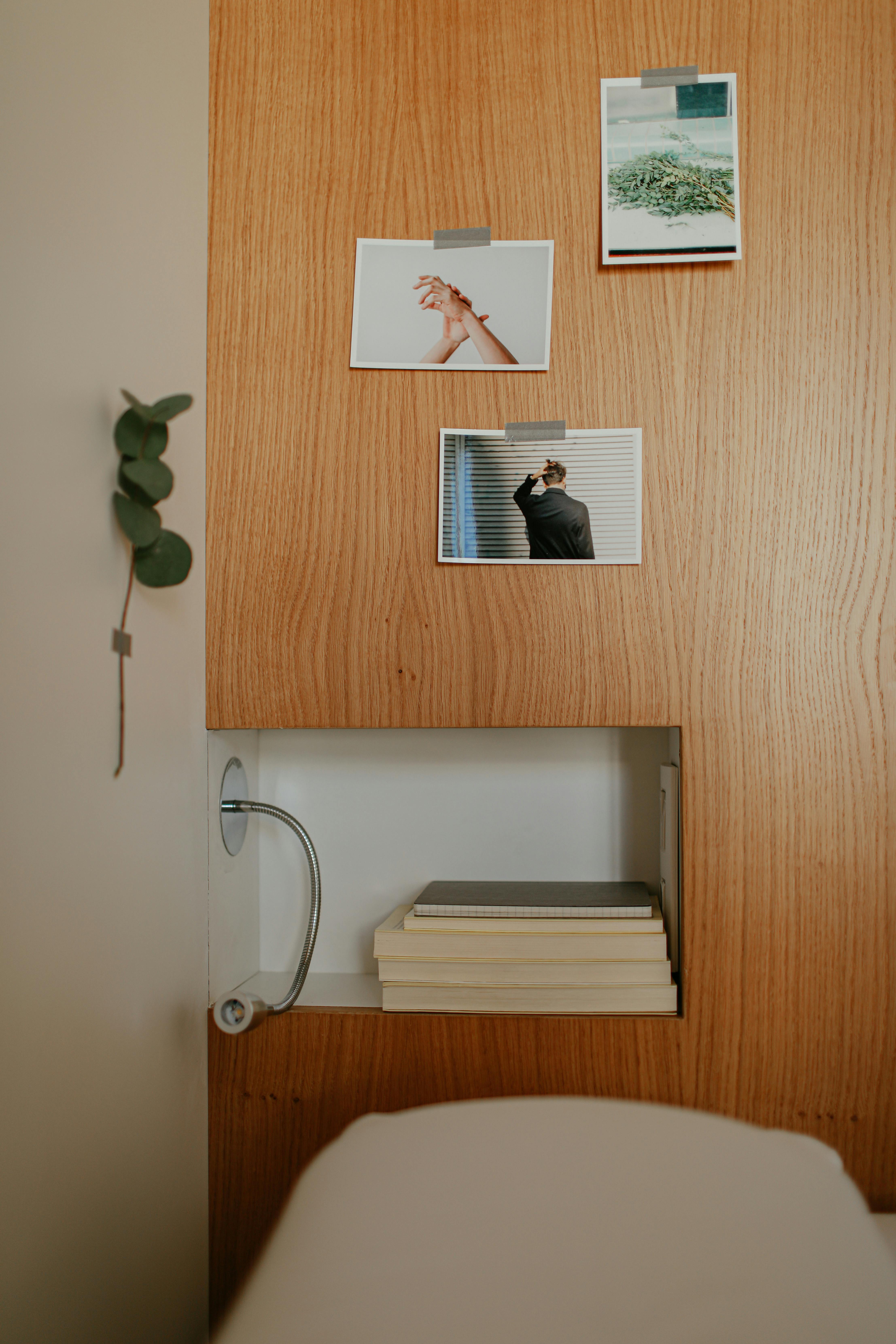 Free A modern wooden shelf with books and taped photographs above, showcasing minimalist design. Stock Photo
