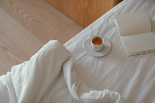 Free A Cup of Coffee and a Notebook on the Bed with White Linen Stock Photo