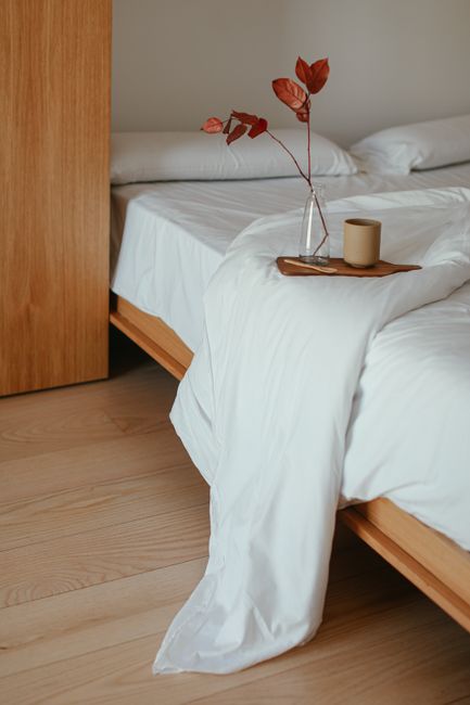 Cozy minimalist bedroom with a tray and vase on a white blanket.