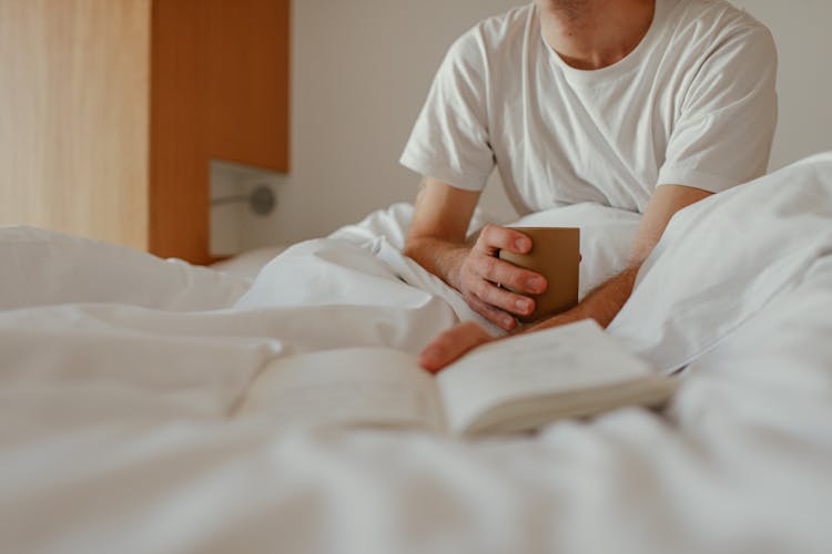 Person In Bed Holding A Cup And A Book