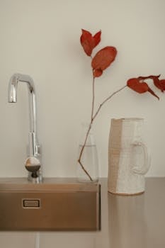Close-up of minimalist kitchen decor with ceramic jug, chrome faucet, and decorative branch.