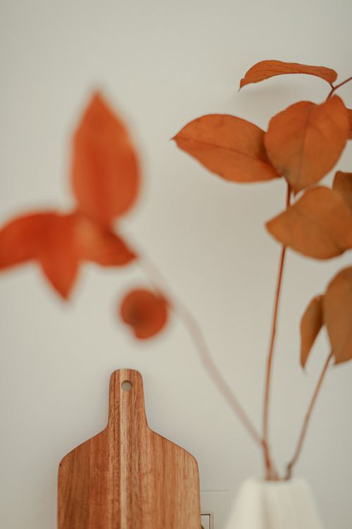 Free Simple autumn decor featuring a wooden cutting board and vase with fall leaves. Warm and cozy vibe. Stock Photo