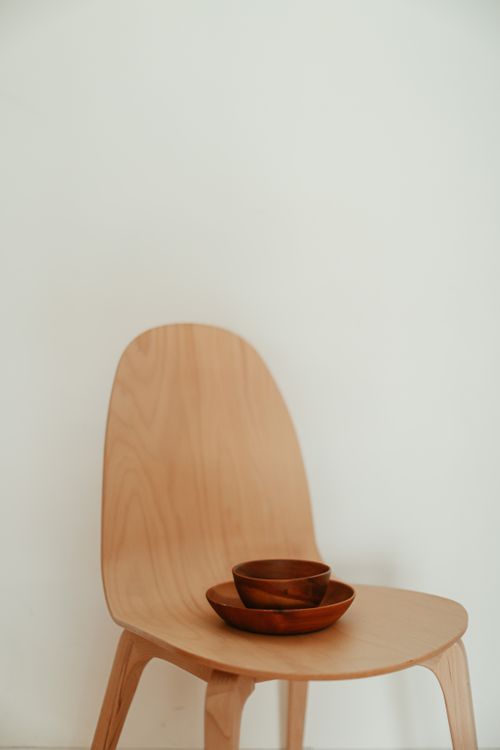 Free A simple, elegant setup featuring a wooden chair and stacked bowls against a white wall. Stock Photo