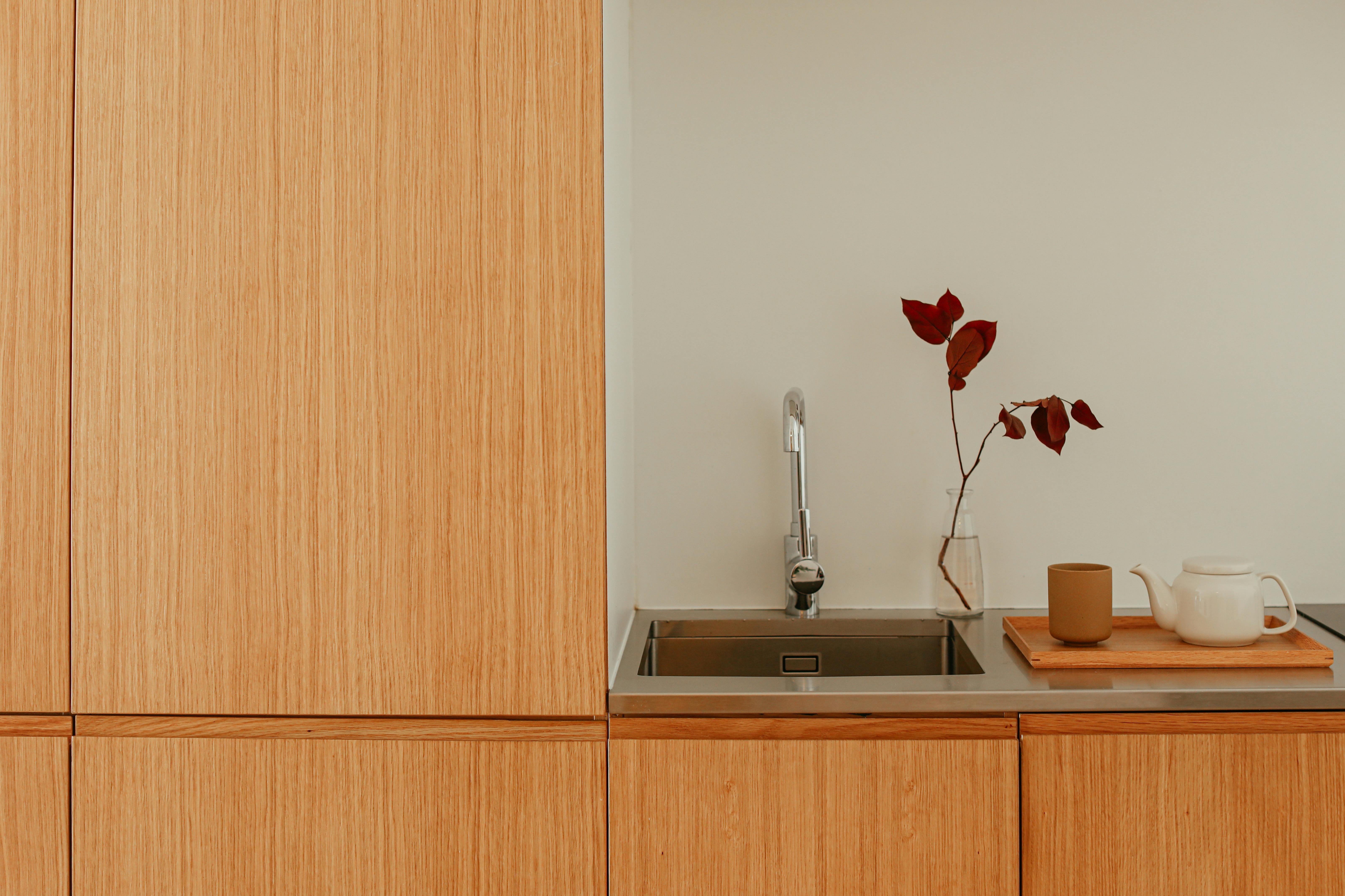 A minimalist kitchen countertop with a sink, teapot, cup, and vase of leaves.