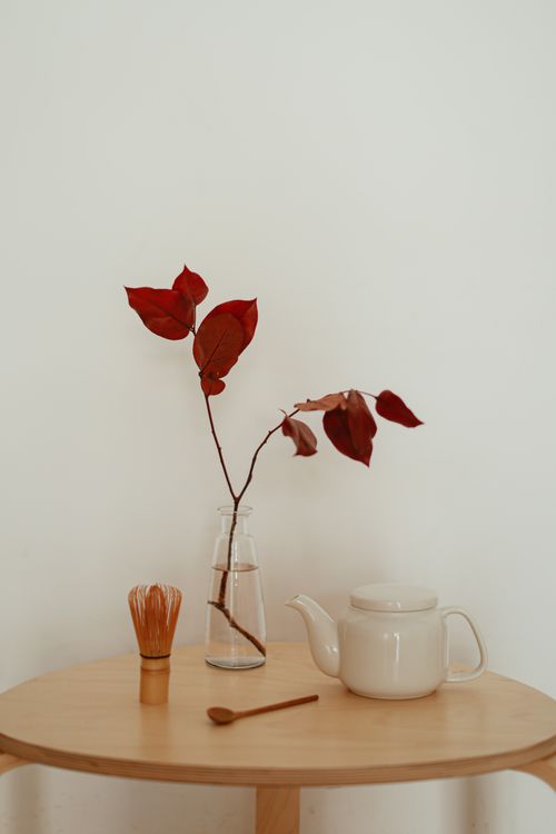Free Elegant minimalist setup featuring a teapot, wooden table, vase with twigs, and bamboo whisk. Stock Photo