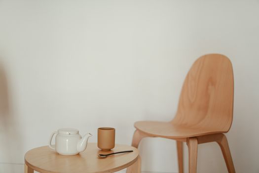 Simple, elegant scene with a wooden table, teapot, and chair in a minimalist setting.