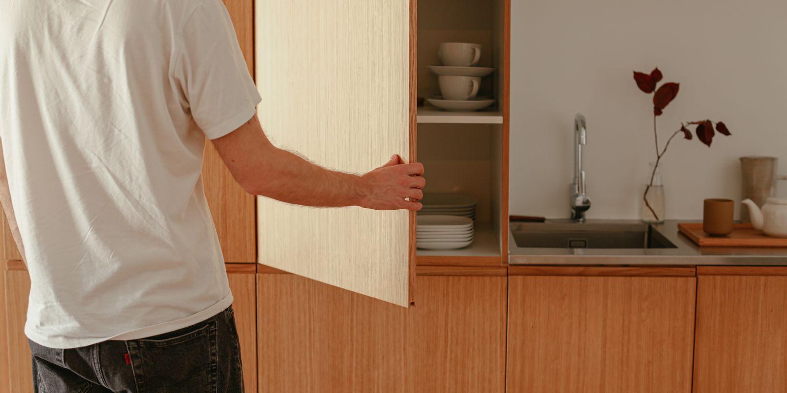 A man opens a wooden kitchen cabinet in a modern minimalist kitchen.