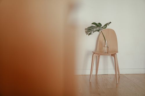 Free A minimalist setup featuring a wooden chair with a glass vase and plant leaf. Stock Photo