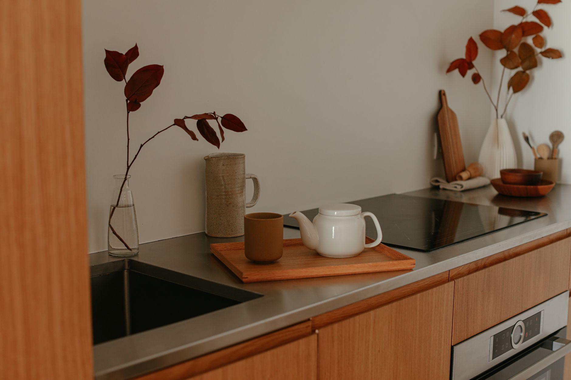 A minimalist kitchen countertop featuring a teapot, mug, and autumnal decor in warm tones.