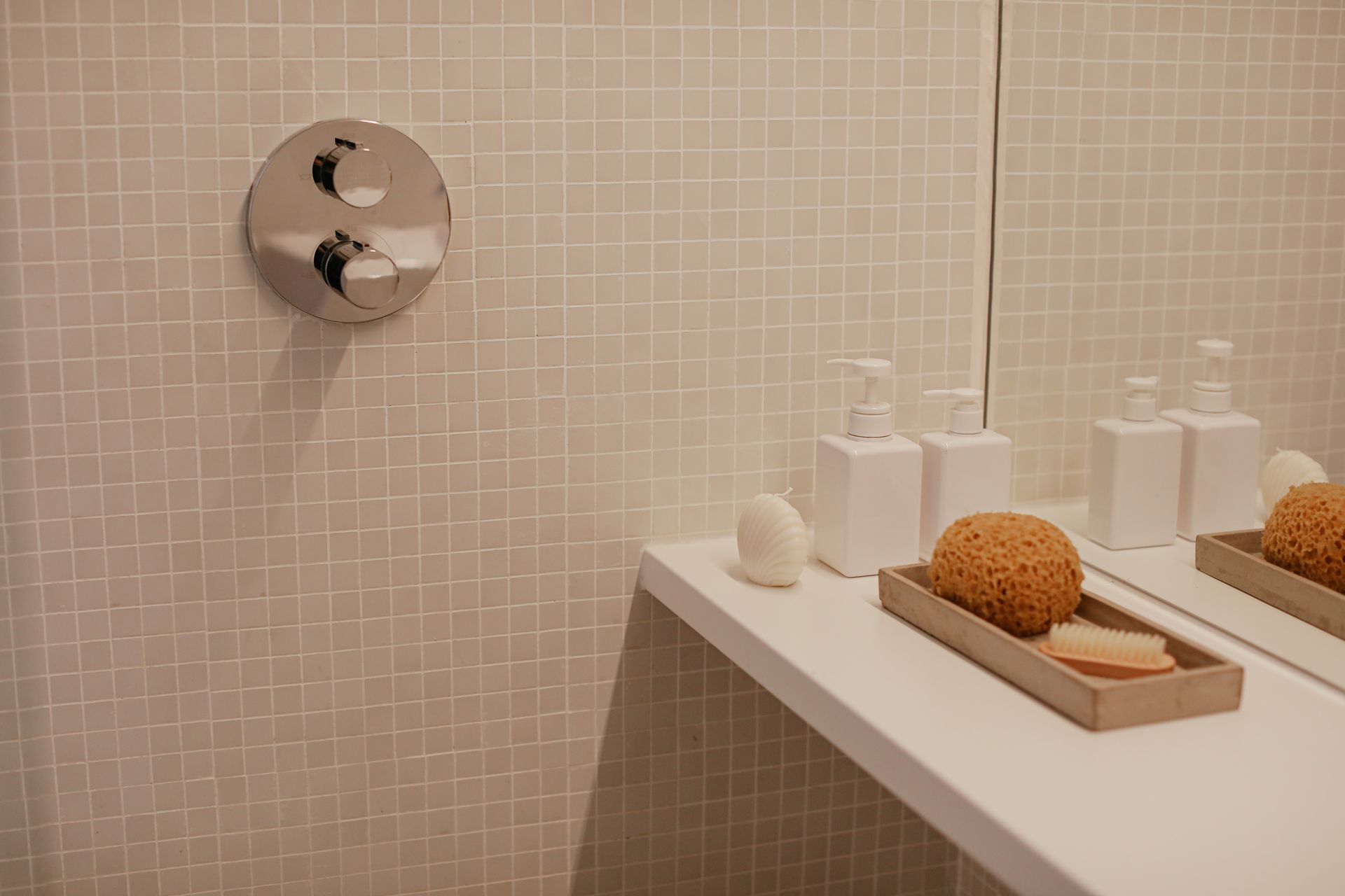 Clean, minimalist bathroom featuring soap dispensers and a loofah on a shelf against a tiled wall.