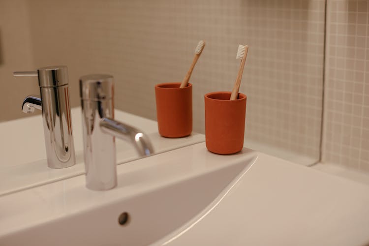 A Red Cup With A Wooden Toothbrush On A Ceramic Sink