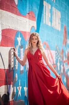 Elegant woman in a red dress posing against a patriotic mural on an urban street.