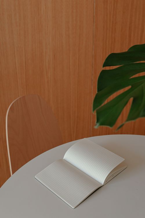 Free Open notebook on a white round table with a green leaf, showcasing minimalism and simplicity. Stock Photo