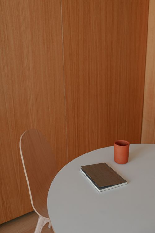 Free Modern minimalist workspace with a notebook and cup on a round white table against a wooden backdrop. Stock Photo