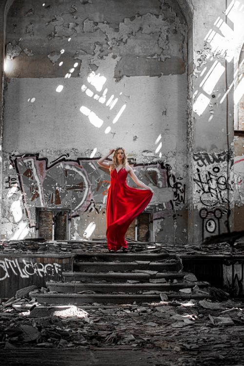 Free A woman in a red dress stands in a graffiti-filled abandoned building, creating a contrast between elegance and decay. Stock Photo
