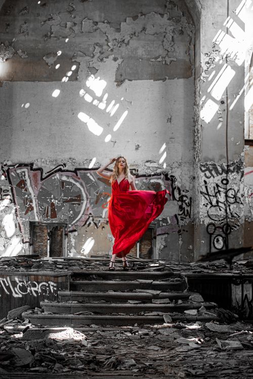 Free A striking woman in a red dress poses amidst the graffiti-covered ruins of an abandoned building. Stock Photo