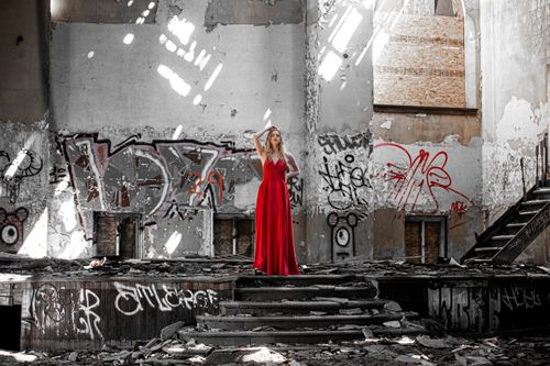 Free Elegant woman in a red dress poses in an abandoned, graffiti-covered building. Stock Photo