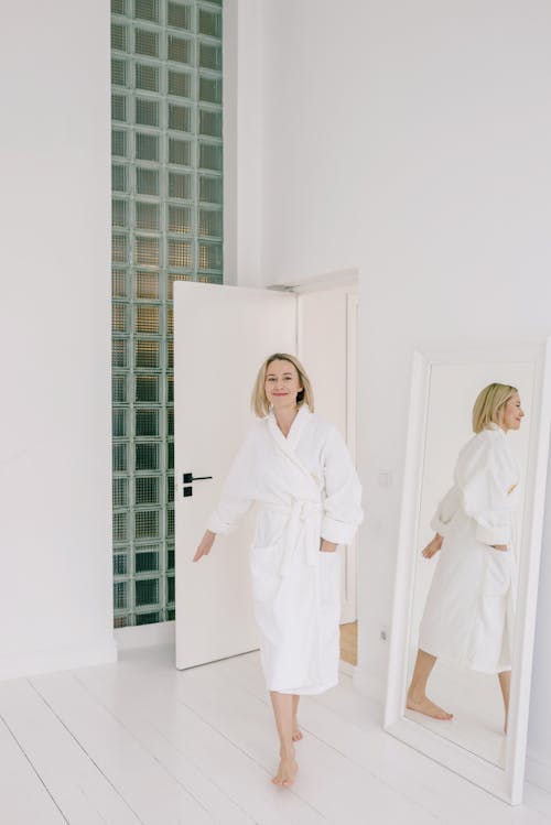 A Woman Wearing a White Bathrobe Walking Past a Mirror