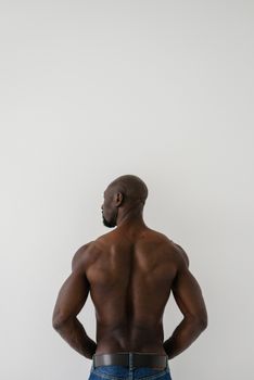 A bald, muscular black man stands topless with his back to the camera, showcasing a strong physique.