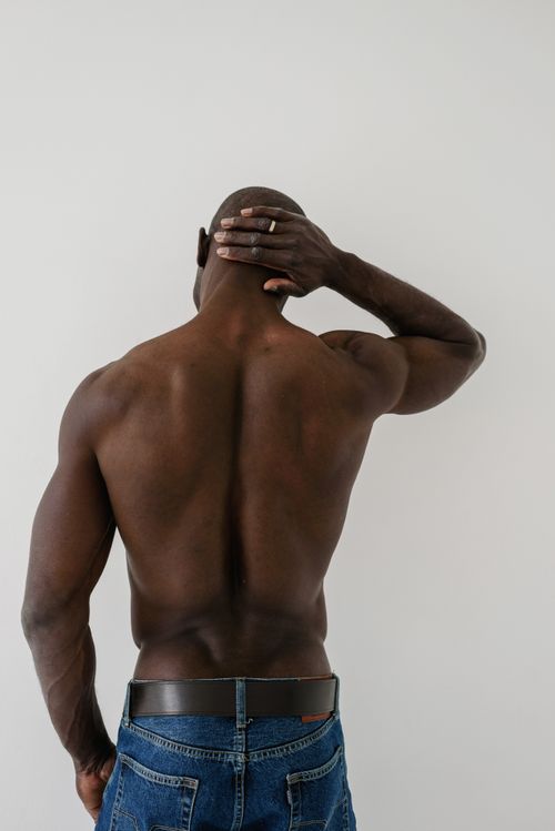 Free A bald man showing his muscular back while wearing denim jeans and holding his head. Stock Photo