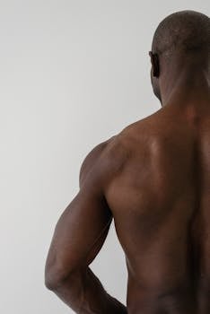 A shirtless muscular black man with toned muscles seen from behind, highlighting a fit physique.