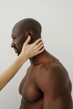 A shirtless, muscular black man with a hand gently placed on his face.