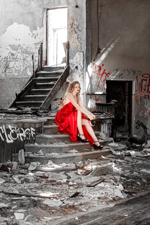 A Woman in Red Dress Sitting on the Stairs of an Abandoned Building