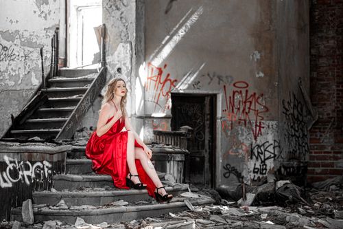 Free Elegant woman in a striking red dress sits in an abandoned building, adding contrast to the dilapidated surroundings. Stock Photo