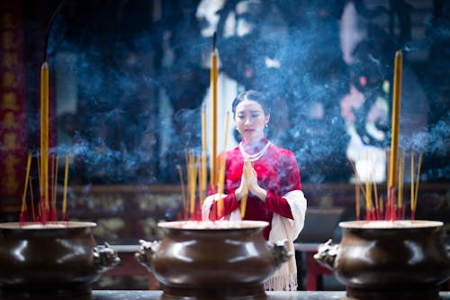 Elegant young Asian woman praying in shrine near burning incense sticks