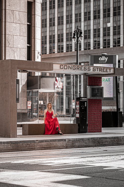 Photograph of a Woman in a Red Dress Sitting at a Bus Stop