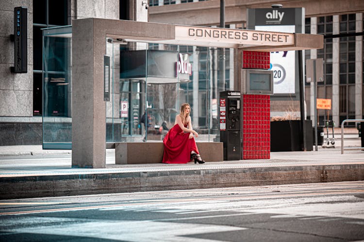 A Woman In Red Dress Sitting Near A Telephone Booth In Congress Street