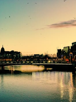 日落时分，都柏林海滨与城市风光的宁静景致，倒映在平静河面上，映照着充满活力的光芒