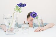 Woman in White Shirt Sitting Beside Table With Purple Flower