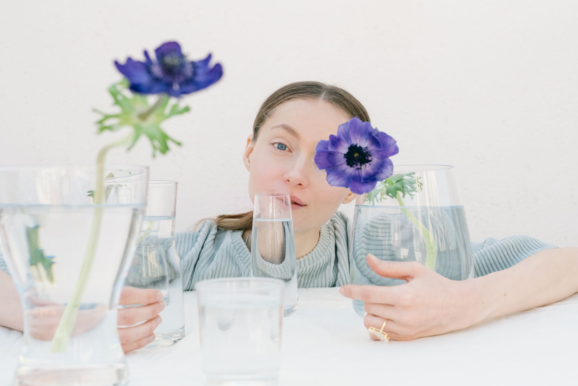 A woman surrounded by purple anemone flowers in vases against a white background.