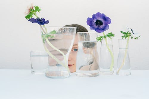 A Woman Behind Glass Vases with Purple Flowers