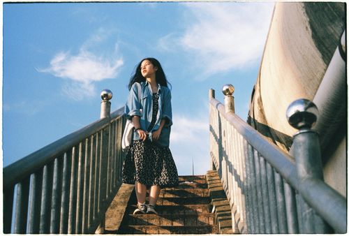 Free A woman stands on concrete stairs outdoors, wearing a denim jacket under a blue sky. Stock Photo