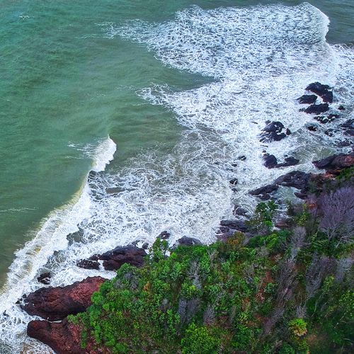Free Aerial shot of a rocky shoreline with crashing waves and lush greenery highlighting a beautiful coastal landscape. Stock Photo