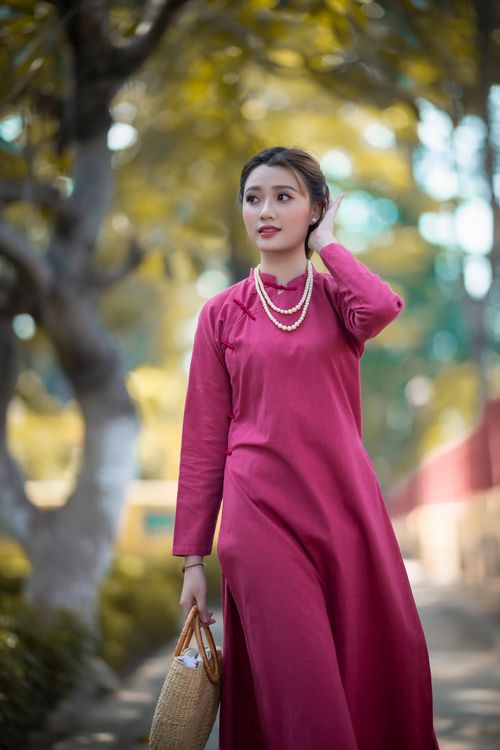 Free Self assured young Asian lady in elegant maxi dress and pearl necklace touching hair and looking away while walking in park on sunny day Stock Photo