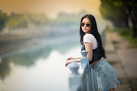Trendy young Asian woman leaning on fence at riverside in park