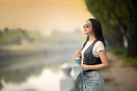 Self assured young ethnic lady standing near river under sundown sky