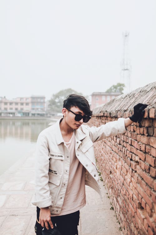 Free Photo of a Man with Black Sunglasses Leaning on a Brick Wall Stock Photo