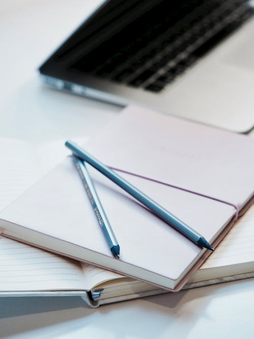 Two Blue Pencil on Top of White Notebook