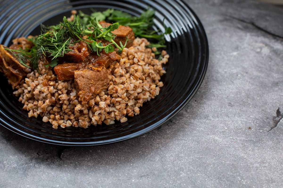 Toasted buckwheat on a black plate with braised beef chunks, fresh dill and greens