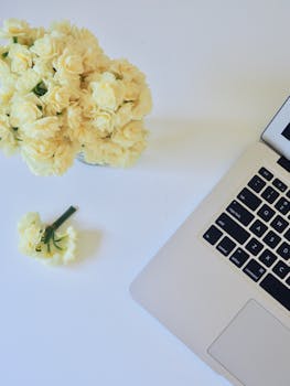 Minimalist workspace with bouquet of flowers and a laptop on a white desk.