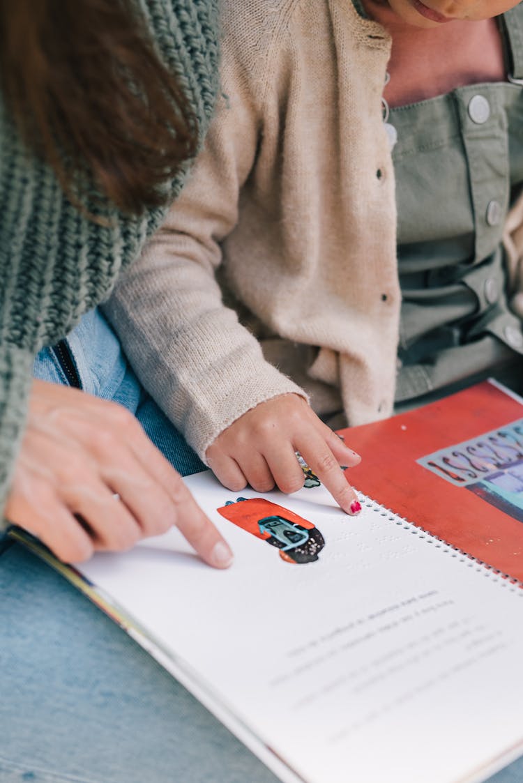 Close-up Of Mother And Daughter Reading A Story In Braille 