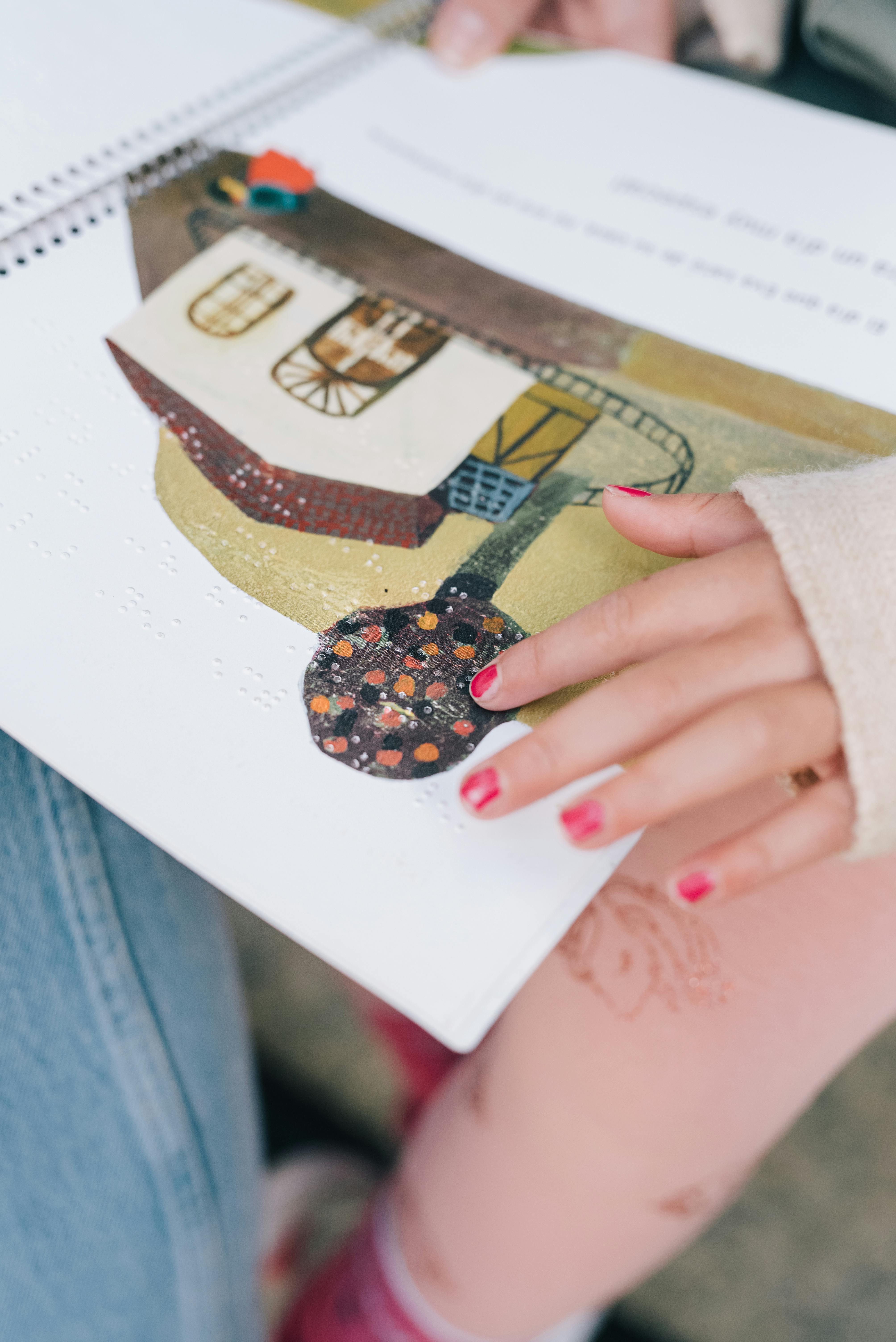 Close-up of hands reading a braille book with a colorful illustration. Ideal for learning and accessibility themes.