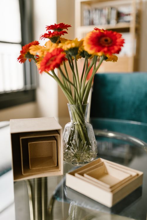 Free Bright gerbera daisies paired with cardboard boxes on a glass table. Stock Photo