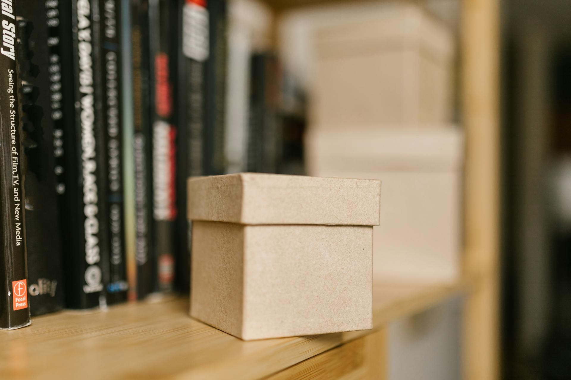 Close-up shot of a small brown paper box on a wooden shelf with books in the background.