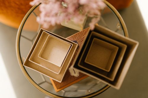 Free Artistic flat lay of stylish nested cardboard boxes on a glass table with blurred flowers in the background. Stock Photo