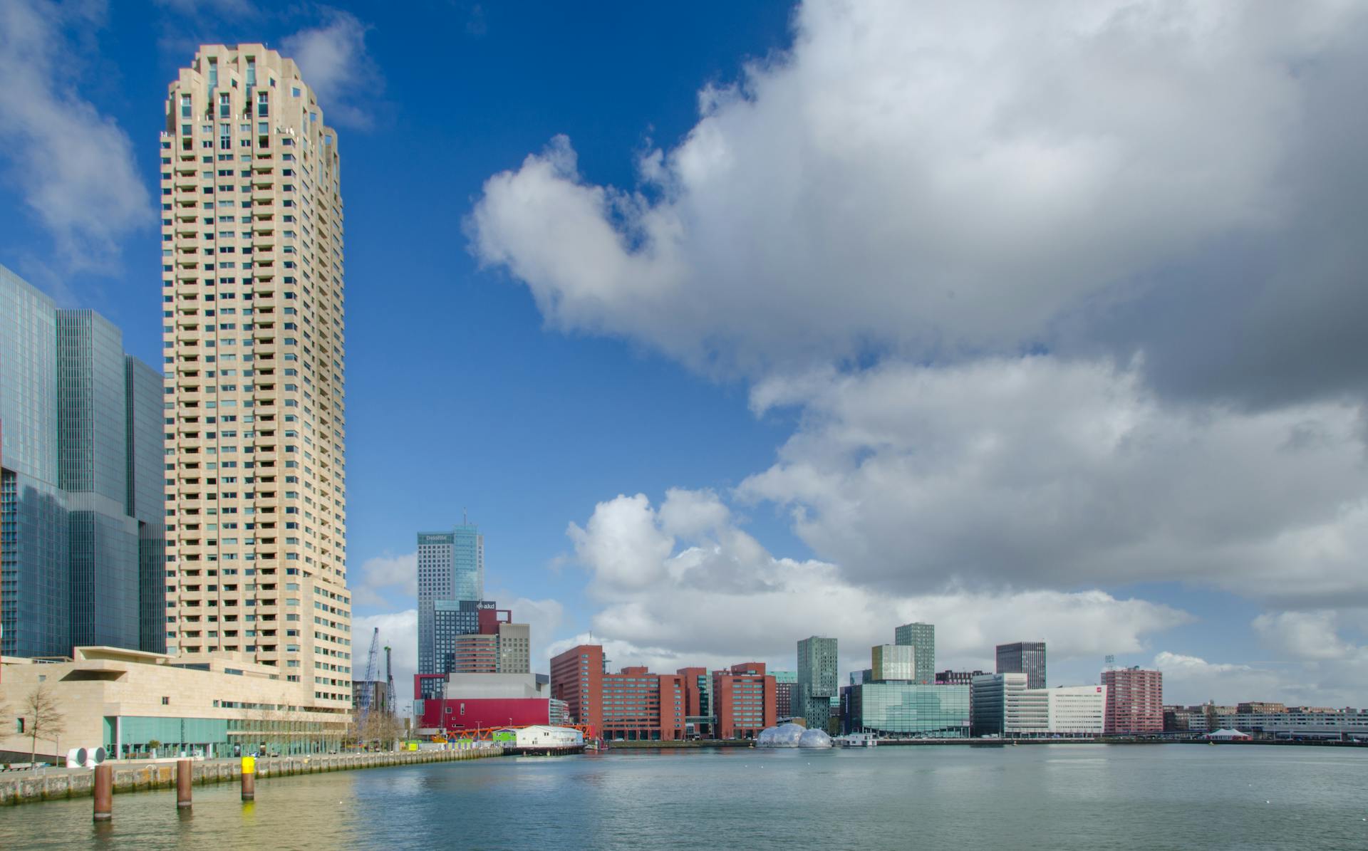 Explore the modern cityscape of Rotterdam featuring skyscrapers and waterfront views under a blue sky.